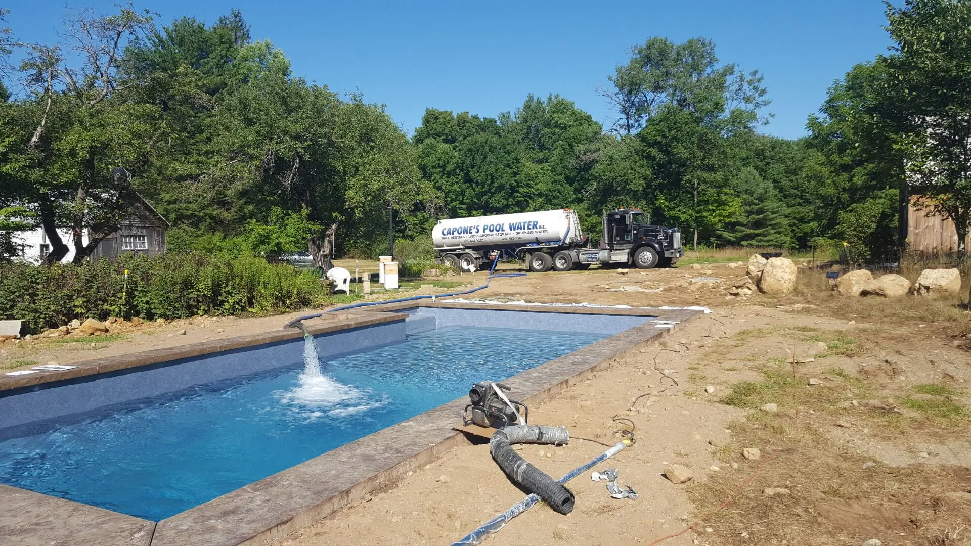 A pool being cleaned by a truck and some people.